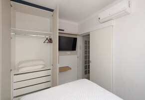 A bedroom with a bed, a wardrobe, a television, and a door leading to another room.