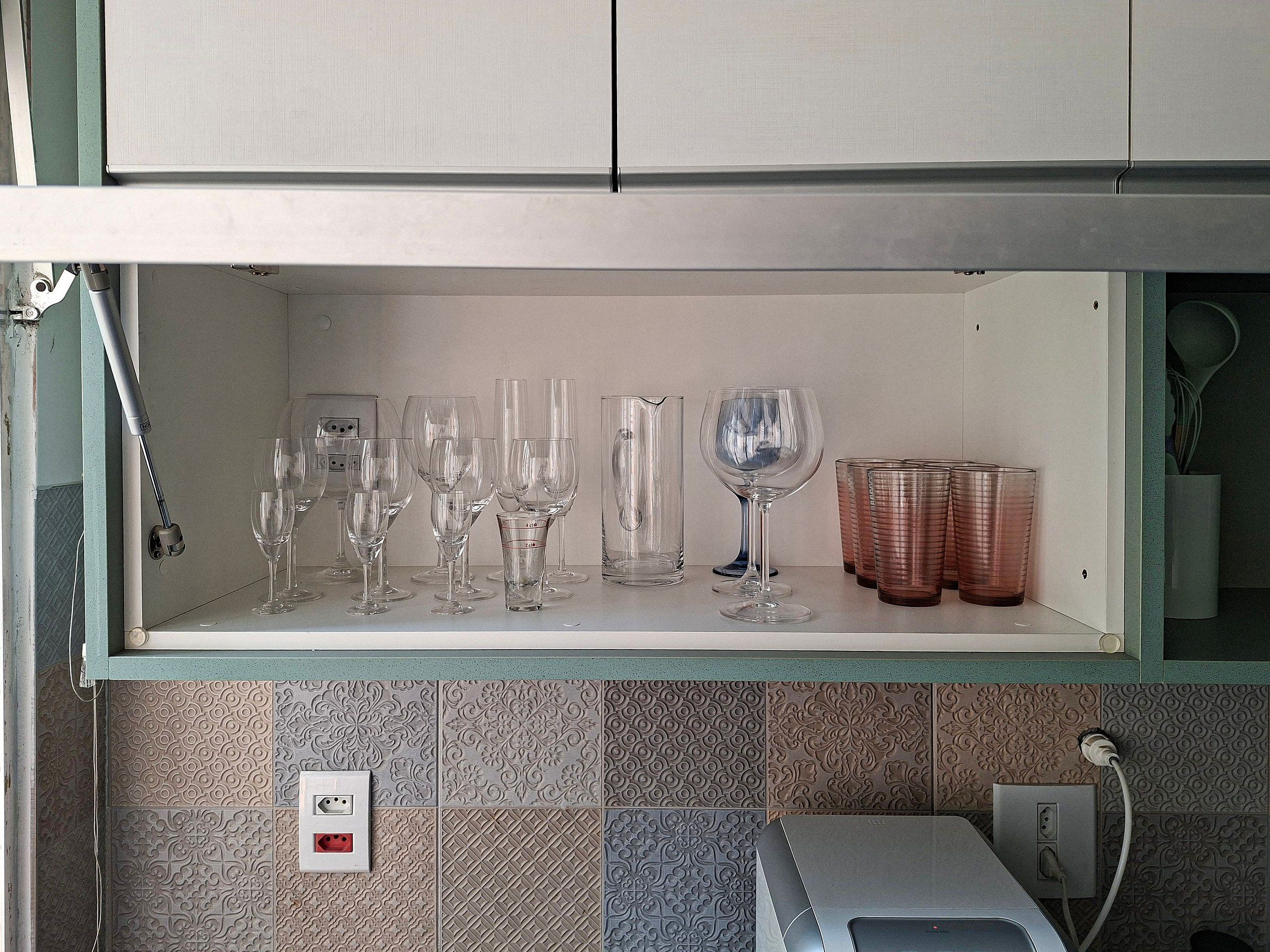 Une cuisine avec une étagère où sont rangés différents types de verres, notamment des verres à vin et des verres à cocktail.