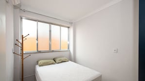 A bedroom with a bed, a window, and a coat rack.