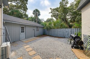 Ein Garten mit einer gepflegten Schotterterrasse, einem Holzzaun und einem Grill.