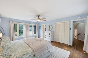 Un dormitorio con cama, cómoda, ventilador de techo y vistas al exterior a través de una ventana.