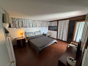 Un dormitorio con cama, mesita de noche, cómoda, ventana con cortinas y puerta.