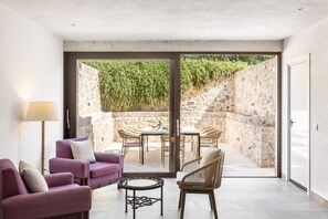 Een modern interieur met een bank, stoelen en een tafel, dat uitkomt op een buitenruimte met een stenen muur en groen.