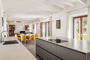 A modern kitchen with a central island, dining area with yellow chairs, and large windows. - Son Barba Mallorca – Private Villa (Sa Pobla)