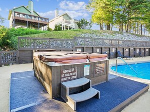 Un bain à remous agrémenté d’un panneau d’avertissement, une piscine et une clôture en bois avec des chaises.