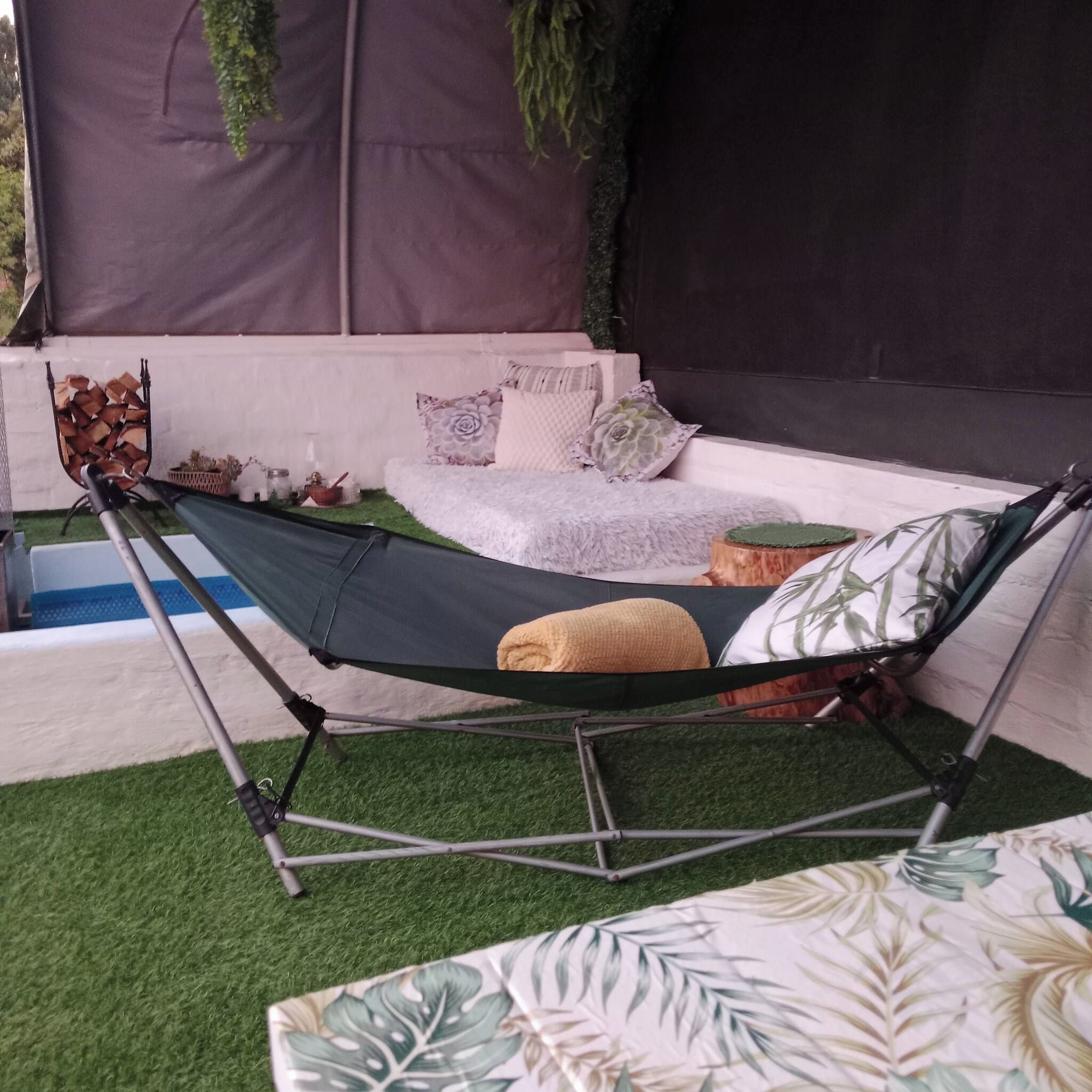 Un sillón hamaca con cojín, un pequeño sofá blanco con cojines estampados y una planta decorativa.