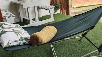A hammock on artificial grass, a white table with a plant, and a bamboo fence.