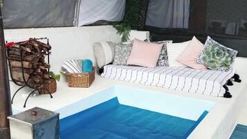 Ein Poolbereich mit einem blauen Pool, einem weißen Sofa mit Kissen, einem Korbwannenkorb und einem Metallbehälter.