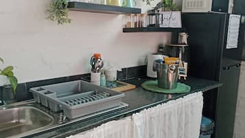 Cocina compacta con lavamanos, microondas y refrigerador. Hay repisas sobre la encimera con varios utensilios de cocina.