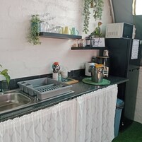 Cocina compacta con lavamanos, microondas y refrigerador. Hay repisas sobre la encimera con varios utensilios de cocina.