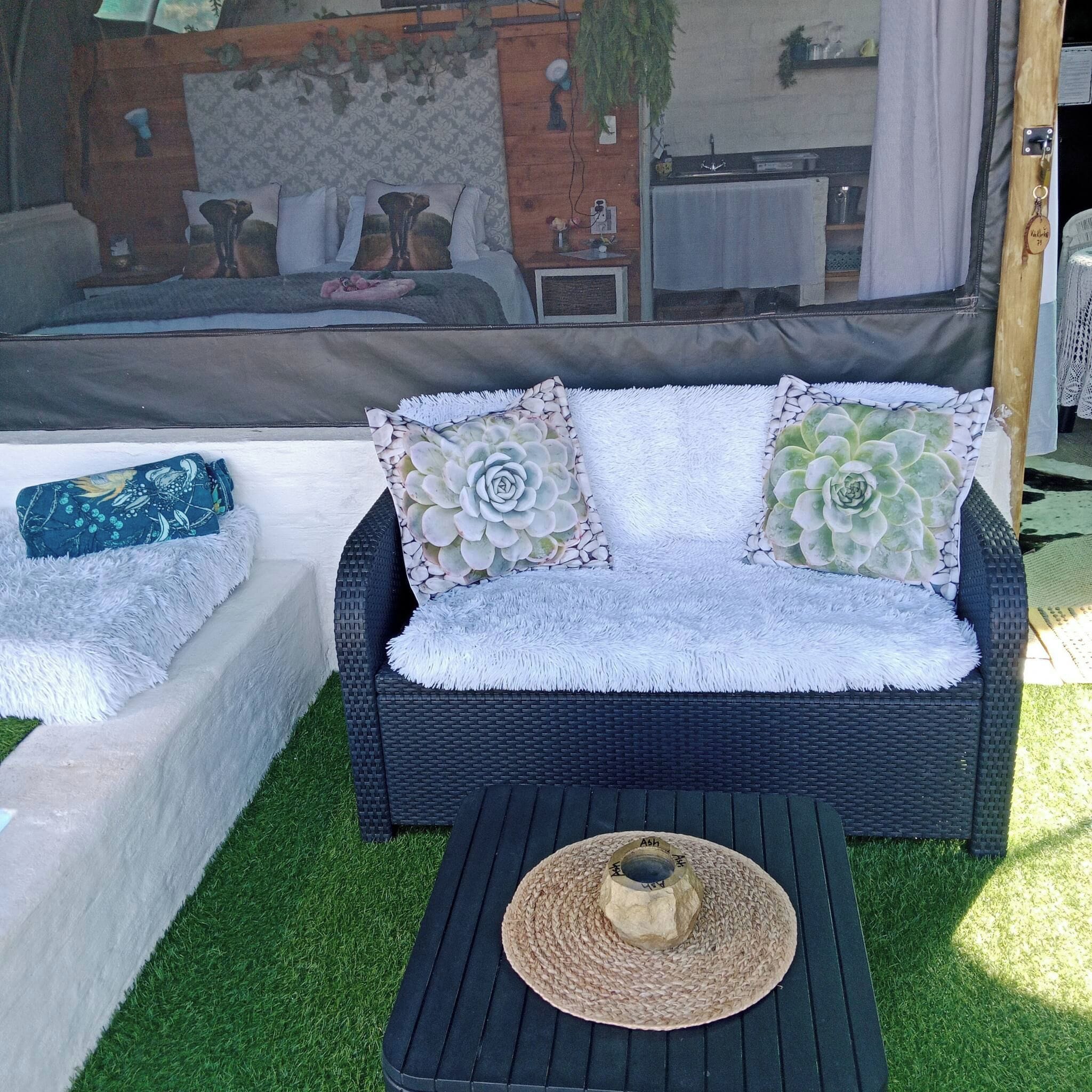 A wicker sofa with patterned cushions, a woven mat, and a small table with a hat.