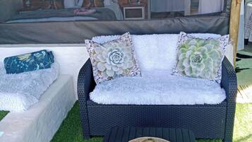 A wicker sofa with patterned cushions, a woven mat, and a small table with a hat.