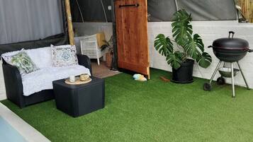 Una carpa con interior blanco, una parrilla negra y una planta en maceta.