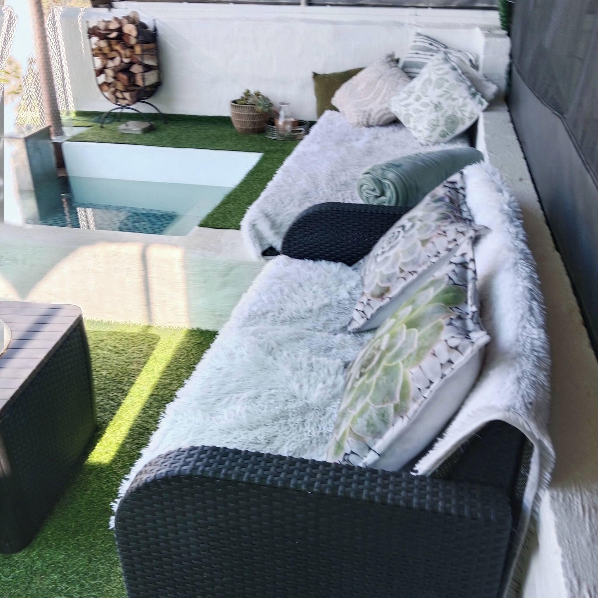 A cozy outdoor seating area with a sofa, cushions, and a small table.