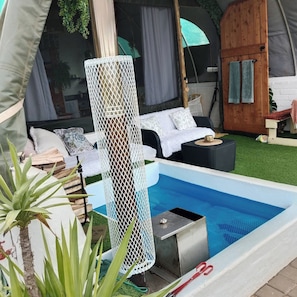 Uma tenda com piscina, móveis brancos e uma rede.
