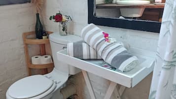A bathroom with a toilet, a shelf with toiletries, a towel, and a mirror.