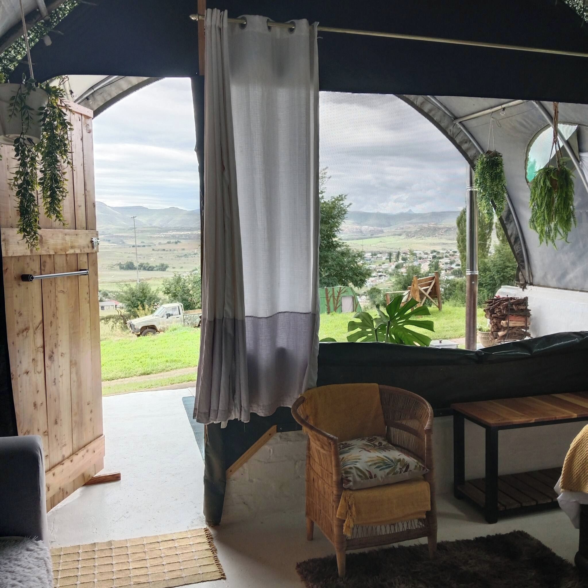 Una habitación con toldo que ofrece vista a un paisaje rural, una silla de mimbre, una puerta de madera y una planta colgante.