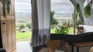 Una habitación con toldo que ofrece vista a un paisaje rural, una silla de mimbre, una puerta de madera y una planta colgante.