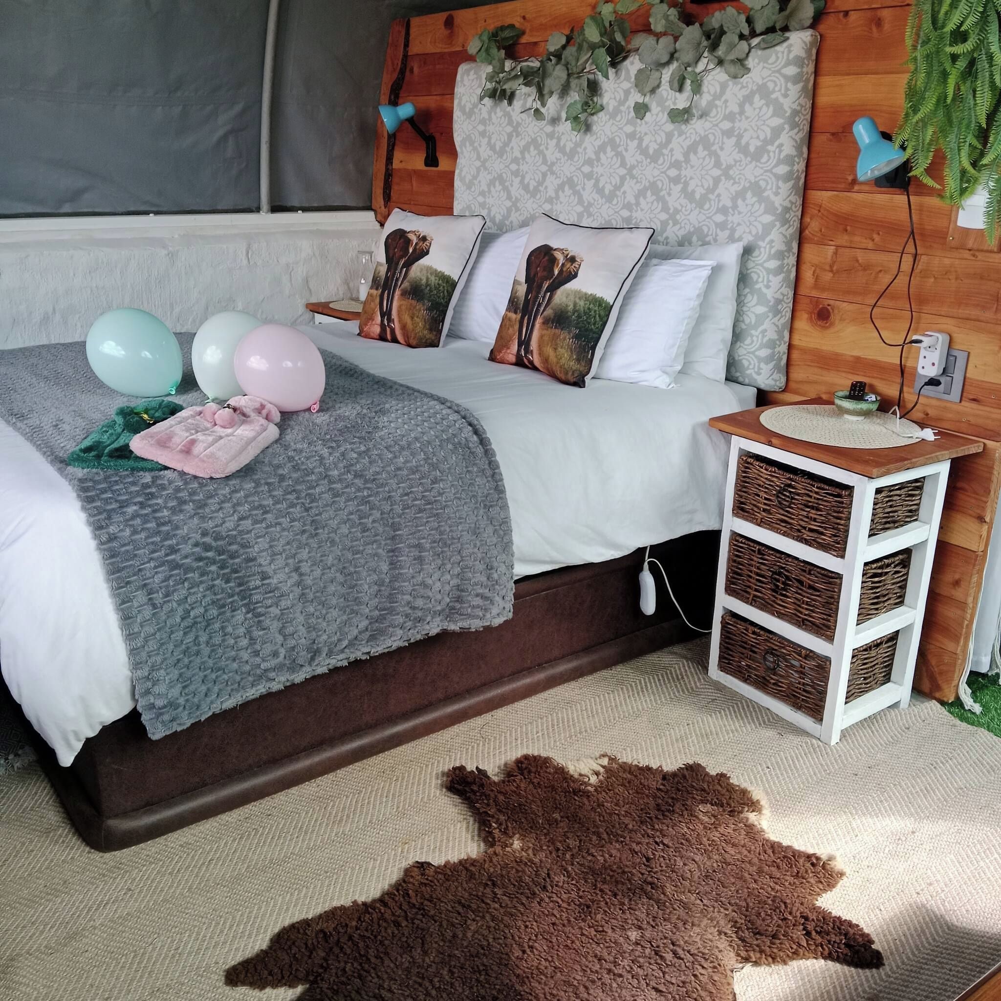 Un dormitorio con cama, almohadas, una colcha, una mesita de noche con lámpara y un enchufe en la pared.