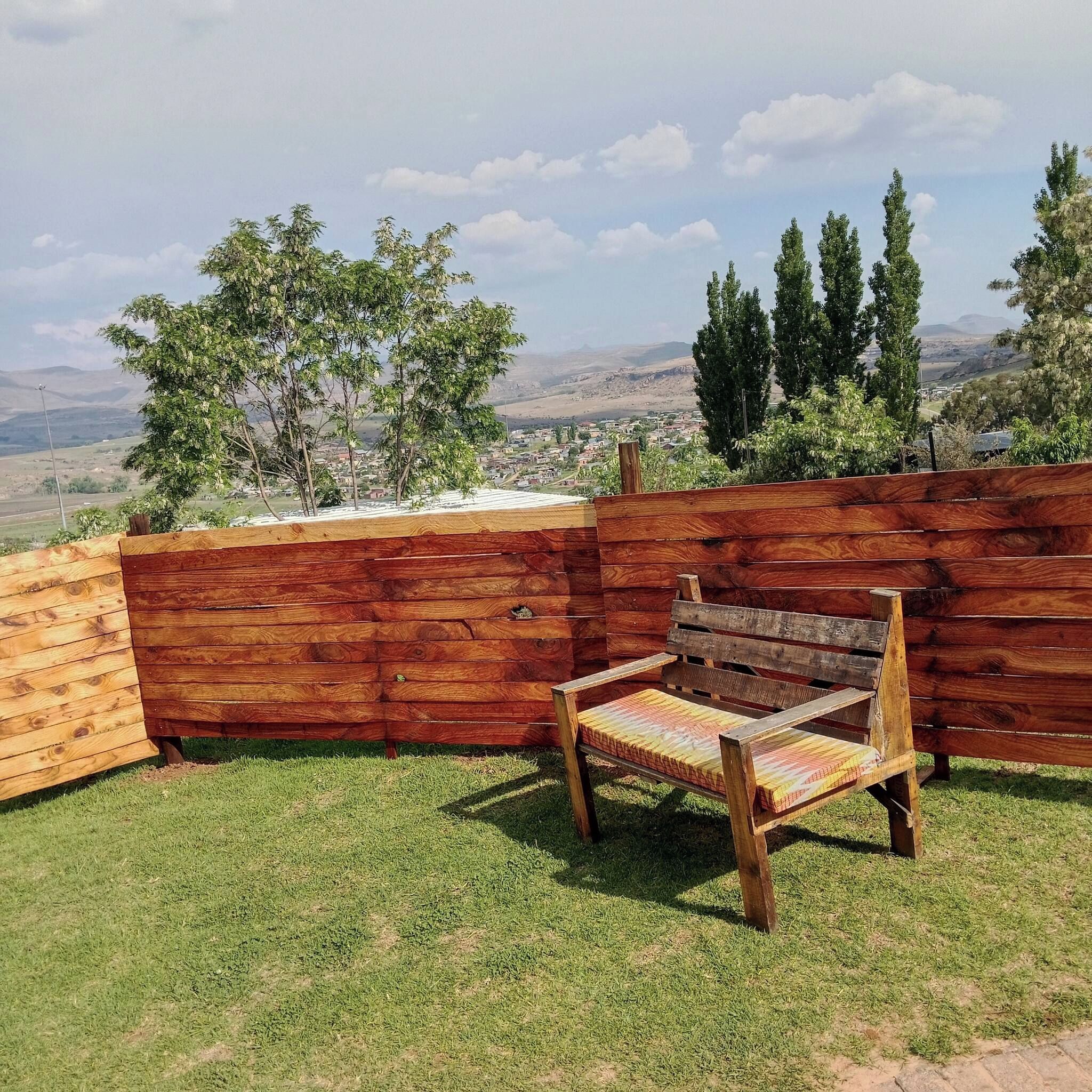 A wooden bench in a grassy outdoor area with a view of a town and hills in the distance.