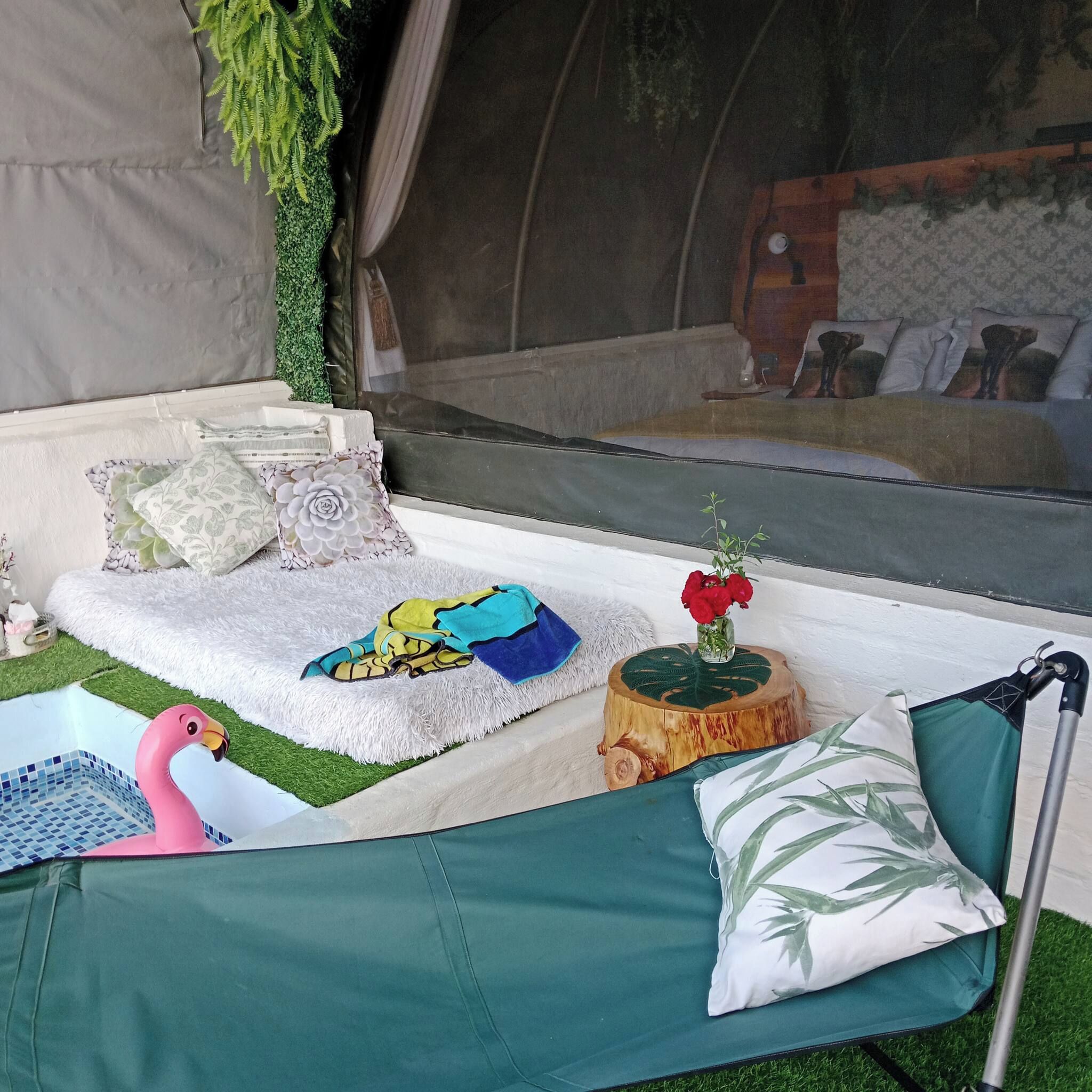 Un espacio al aire libre con carpas, un sofá, almohadones, una mesita con una planta y una decoración de flamenco.