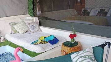 Un espacio al aire libre con carpas, un sofá, almohadones, una mesita con una planta y una decoración de flamenco.