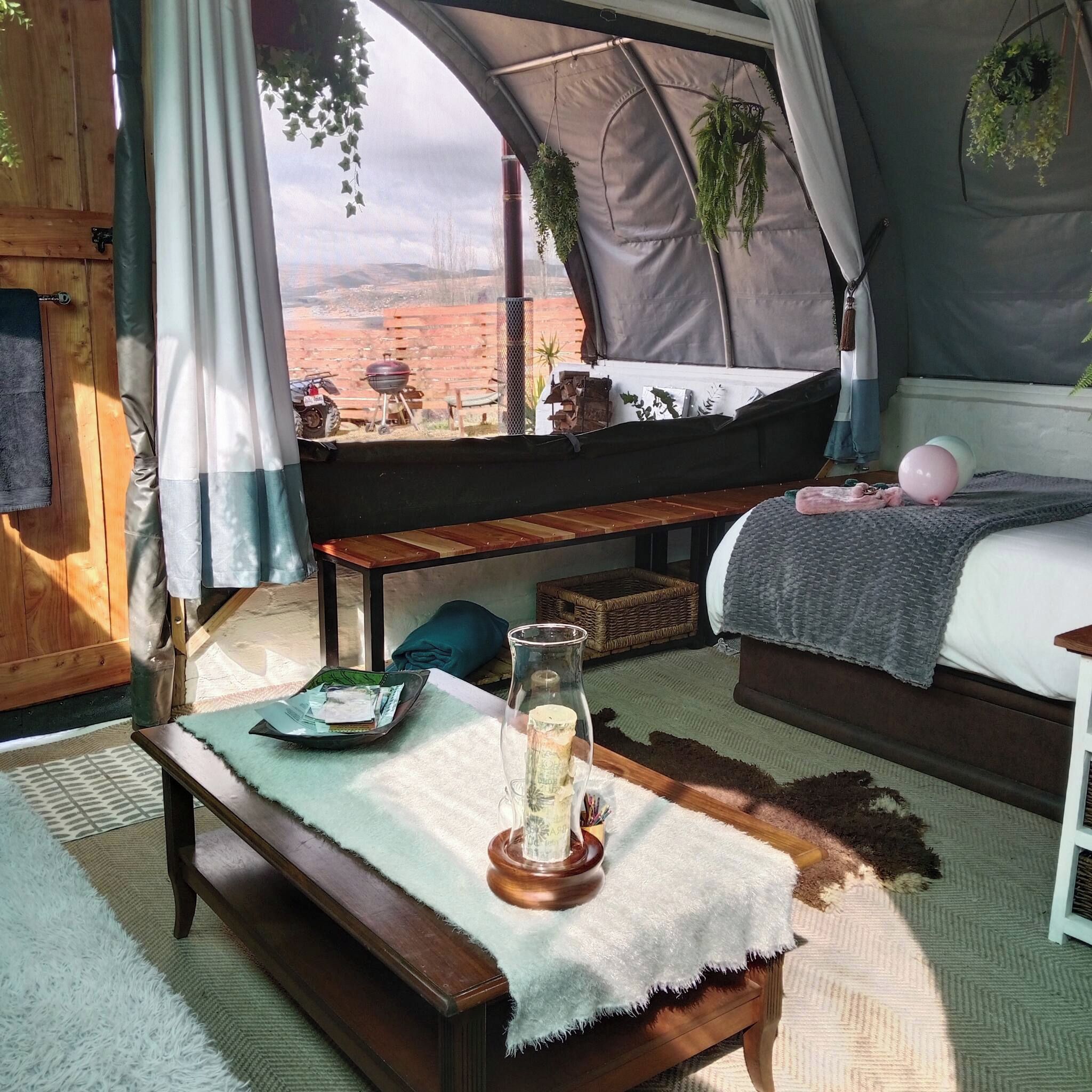 A tented accommodation with a bed, a table with a candle, and a view of the outdoors.
