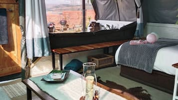 A tented accommodation with a bed, a table with a candle, and a view of the outdoors.