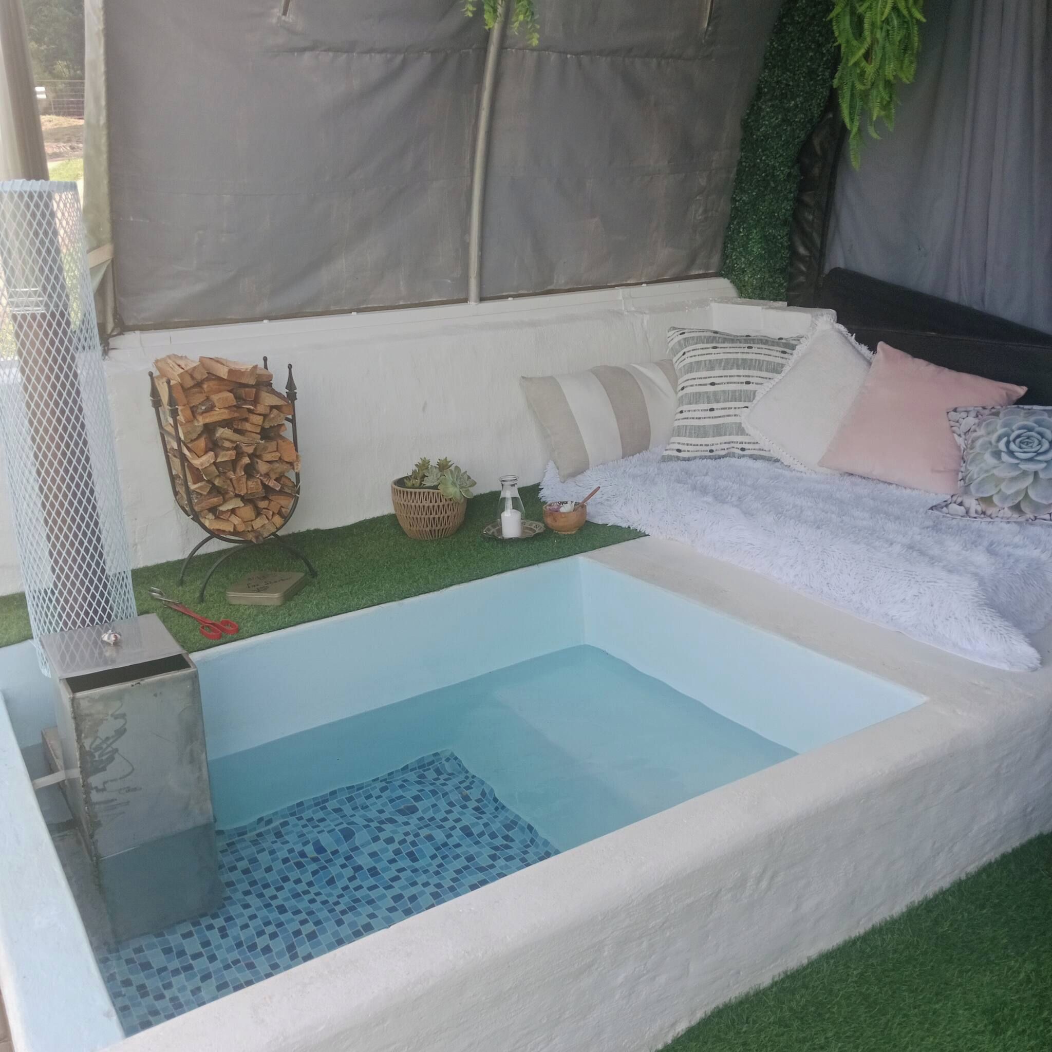 A small, rectangular hot tub with a tiled floor, surrounded by a white wall with a grey canopy overhead.
