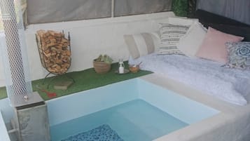 A small, rectangular hot tub with a tiled floor, surrounded by a white wall with a grey canopy overhead.