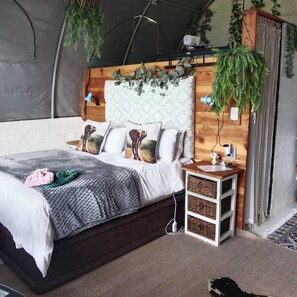 Quarto com tenda, cama, mesas de cabeceira e plantas penduradas.