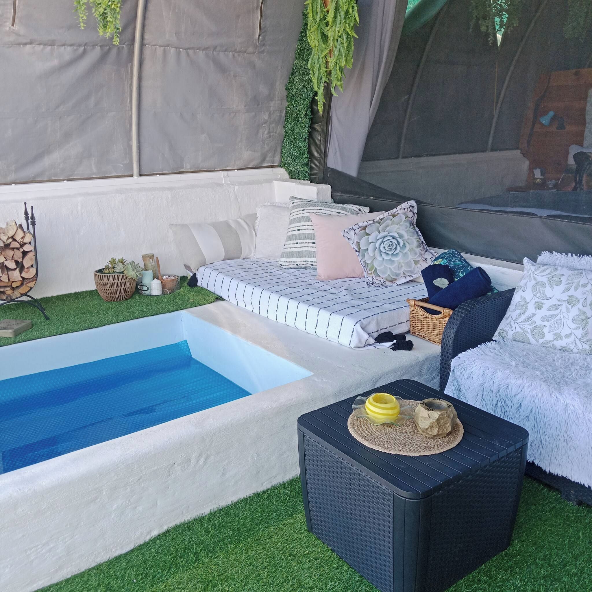 Un área de piscina con piscina blanca y azul, un sofá con cojines y una silla de mimbre.
