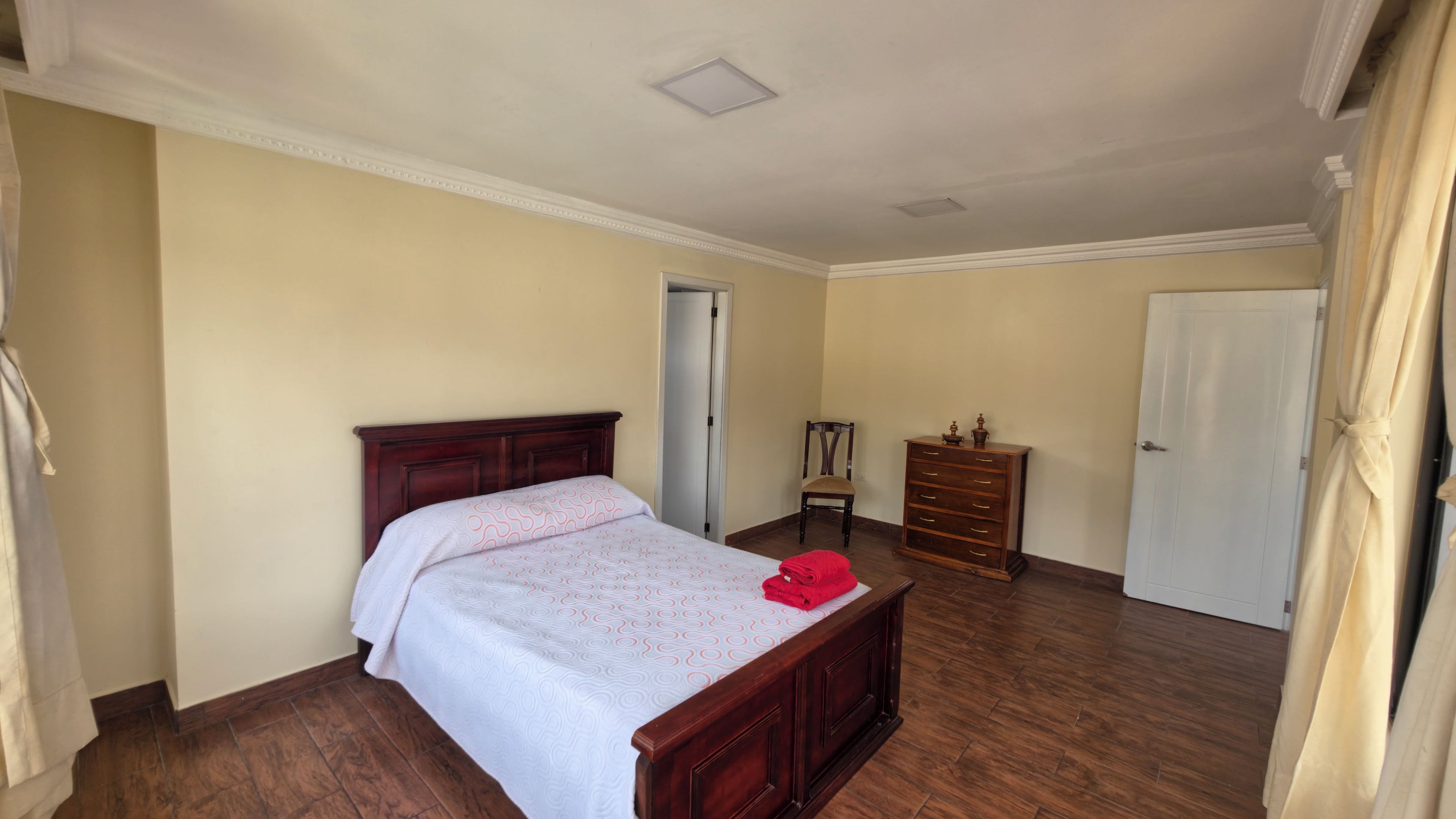 Une chambre à coucher avec un lit en bois, une commode, une chaise et une porte.