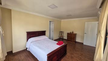 A bedroom with a wooden bed, a dresser, a chair, and a door.