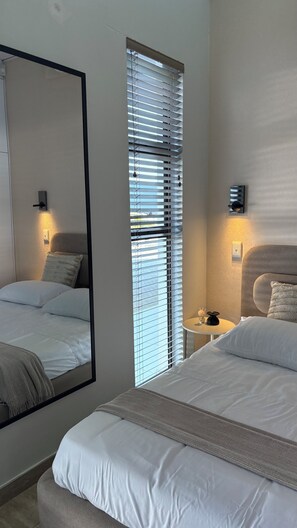 Une chambre à coucher avec un lit, une table de chevet, un miroir et une fenêtre avec des stores.