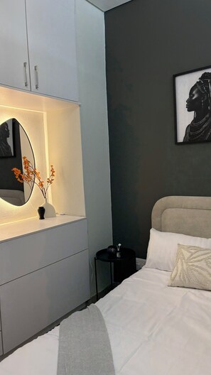 Une chambre à coucher avec un lit, une table de chevet, une commode avec un miroir et un tableau encadré accroché au mur.