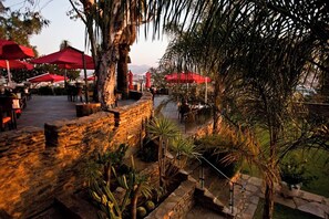 Un espace extérieur aménagé pour les repas, avec des murs en pierre et des parasols rouges.