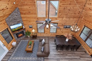 Ein Holzblockhaus-Innenraum mit Kamin, Fernseher, Deckenventilator, Esstisch und Sitzgelegenheit.