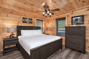 Ein Schlafzimmer mit Holzwänden, einem Bett, Nachttischen, einer Kommode und einem Deckenventilator.