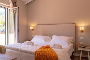 Habitación de hotel con cama, mesita de noche, lámpara y vistas al exterior.