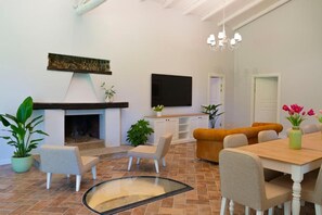 A modern living room with a fireplace, a flat-screen TV, a dining table with chairs, and a sofa. - Villa Cammà with private pool (Mirto)
