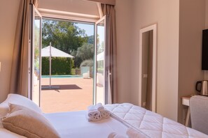 Habitación de hotel con cama, vista al área de piscina exterior y televisor en la pared.
