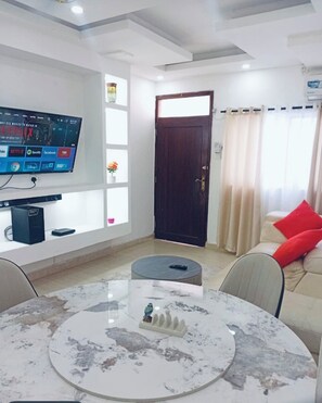 Ein Wohnzimmer mit einem an der Wand montierten Fernseher, einem runden Couchtisch, einem Sofa mit rotem Kissen und einer Tür mit Vorhang.