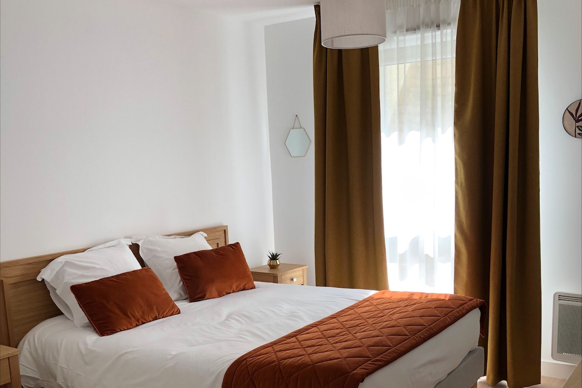 A neatly made bed with a quilted blanket, a bedside table with a lamp, and a window with curtains.