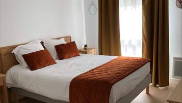 A neatly made bed with a quilted blanket, a bedside table with a lamp, and a window with curtains.