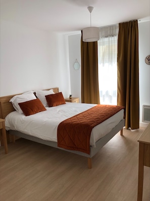 A neatly made bed with a quilted blanket, a bedside table with a lamp, and a window with curtains. - DOMITYS - Les Pierres Dorées (Gleizé)
