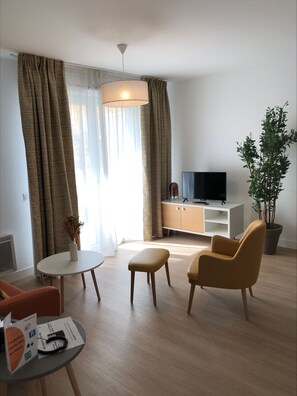 A modern living room with a flat-screen TV, a potted plant, and a dining area with a table and chairs. - DOMITYS - Les Pierres Dorées (Gleizé)