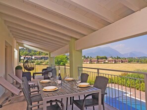 Ein überdachter Essbereich im Freien mit Tisch für zwei Personen, mit Blick auf einen Pool und eine schöne Aussicht auf Berge und ein Feld.
