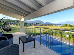 Ein überdachter Außenbereich mit Pool, Sitzgelegenheiten und Blick auf Berge und einen See.