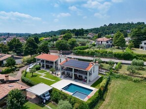 Ein modernes, zweistöckiges Haus mit Swimmingpool, umgeben von üppiger Vegetation und einer hügeligen Landschaft.
